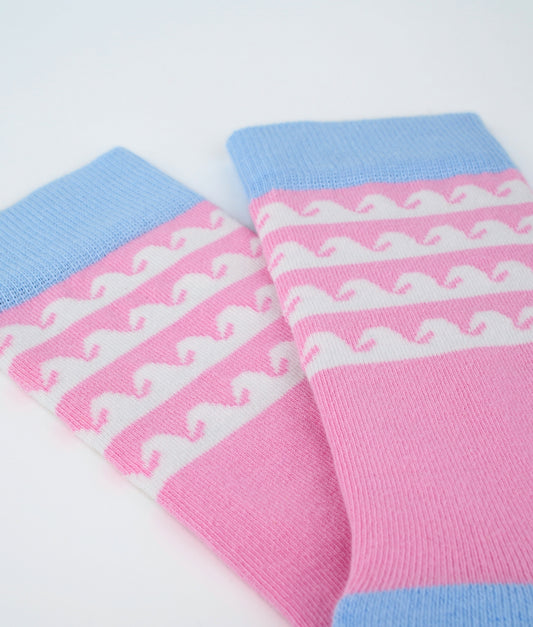 Chaussettes fantaisie roses en coton biologique à motif de vagues blanches. Fabriquées en Europe, elles offrent un confort optimal grâce à leurs zones renforcées et leurs finitions plates sans couture.