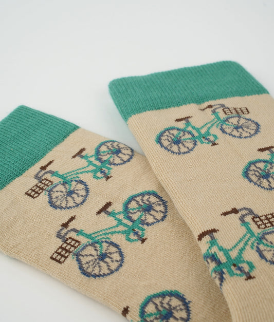 Chaussettes fantaisie vertes et beige en coton biologique à motif de vélos. Fabriquées en Europe, elles offrent un confort optimal grâce à leurs zones renforcées et leurs finitions plates sans couture.