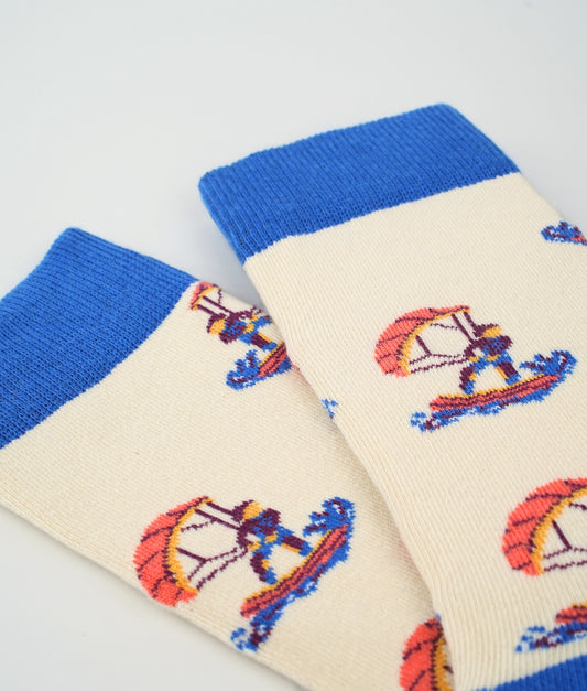 Chaussettes fantaisie beiges et bleues en coton biologique à motif de kitesurfeurs. Fabriquées en Europe, elles offrent un confort optimal grâce à leurs zones renforcées et leurs finitions plates sans couture.