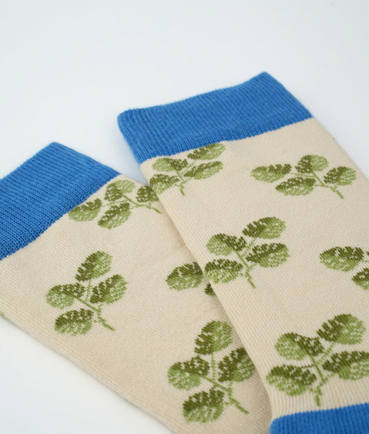Chaussettes fantaisie beiges et bleues en coton biologique à motif de feuilles de Monstera. Fabriquées en Europe, elles offrent un confort optimal grâce à leurs zones renforcées et leurs finitions plates sans couture.