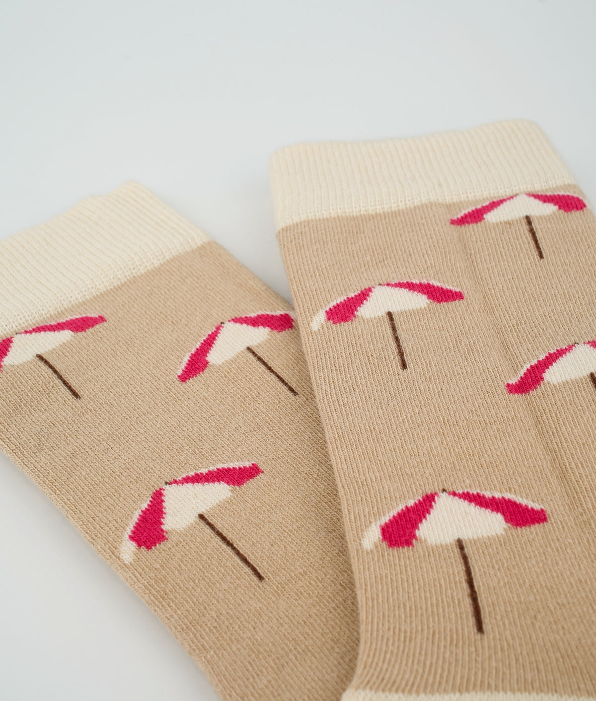 Chaussettes fantaisie beiges en coton biologique à motif de parasols de plage. Fabriquées en Europe, elles offrent un confort optimal grâce à leurs zones renforcées et leurs finitions plates sans couture.