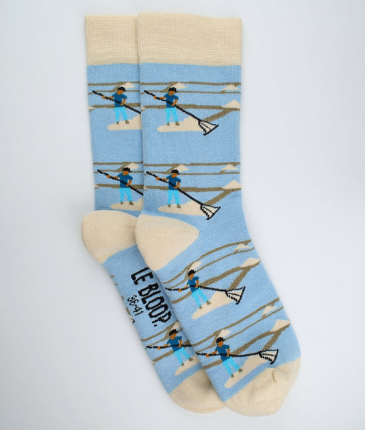 Chaussettes fantaisie bleu clair et beige à motif de sauniers, inspirées des marais salants de l’Atlantique. Fabriquées en Europe en coton biologique, elles offrent confort, douceur et un clin d’œil au savoir-faire local.