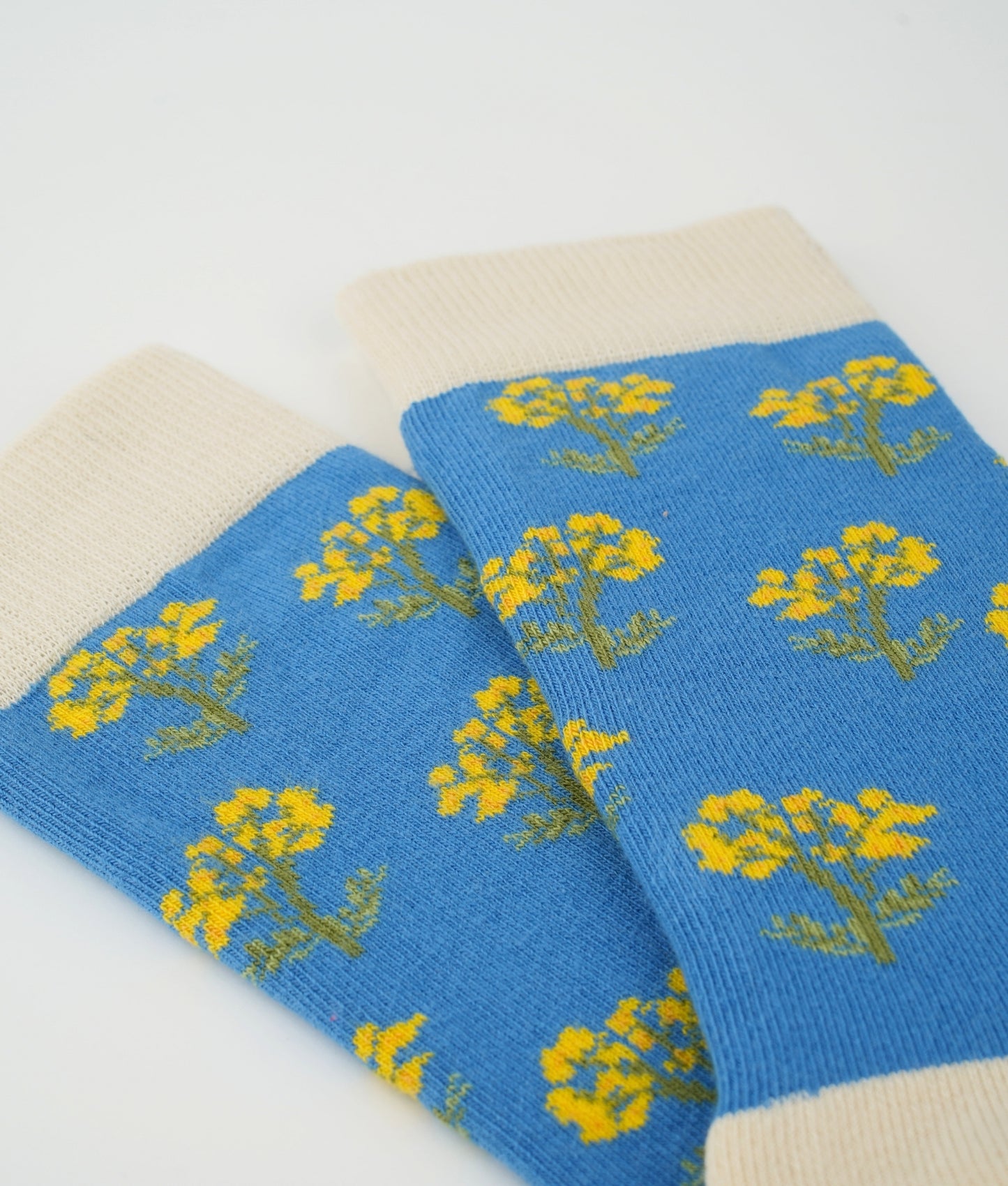 Chaussettes fantaisie bleues en coton biologique à motif de fleurs immortelles. Fabriquées en Europe, elles offrent un confort optimal grâce à leurs zones renforcées et leurs finitions plates sans couture.