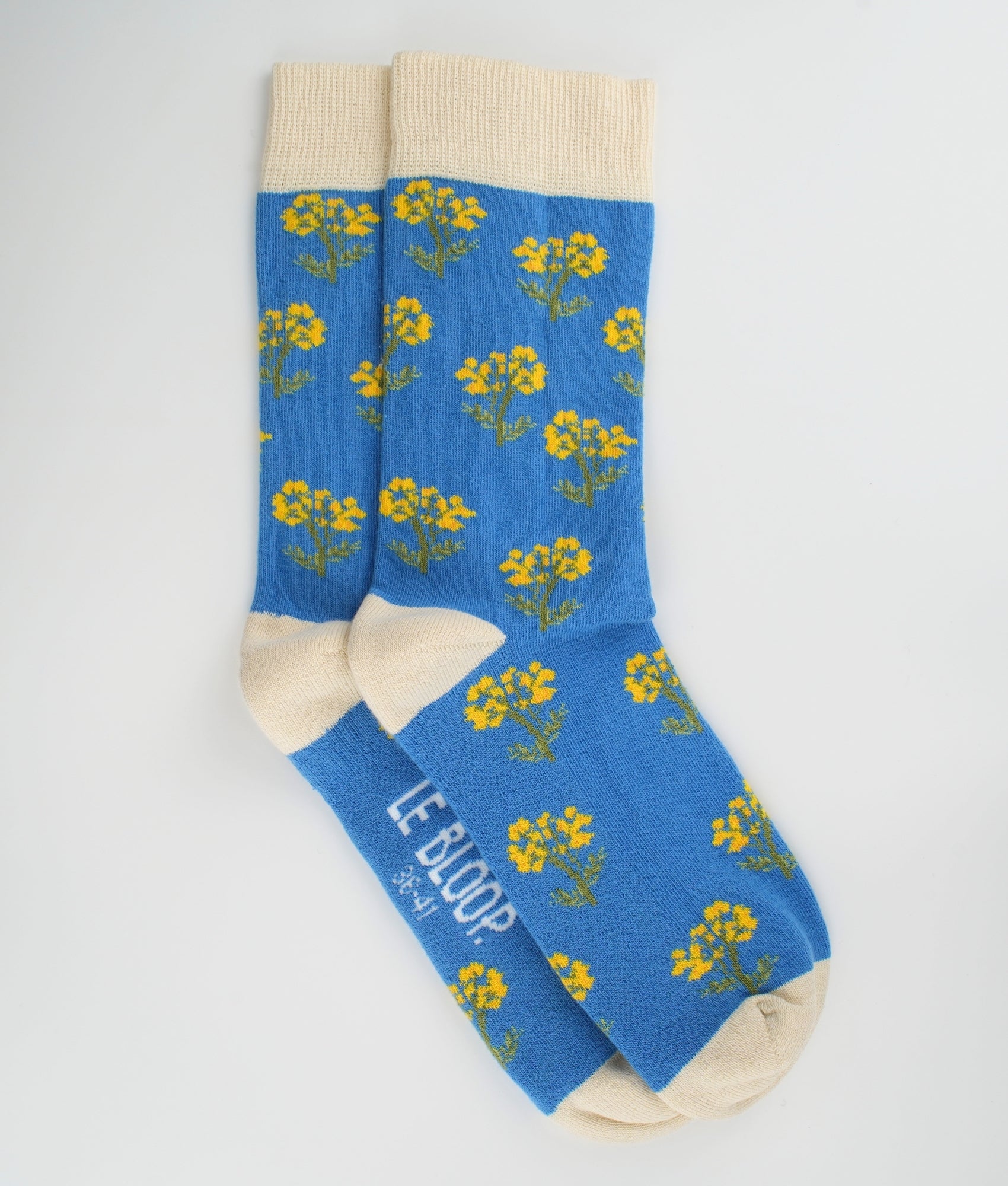 Chaussettes fantaisie bleues et crème en coton biologique à motif de fleurs immortelles. Fabriquées en Europe, elles offrent un confort optimal grâce à leurs zones renforcées et leurs finitions plates sans couture.