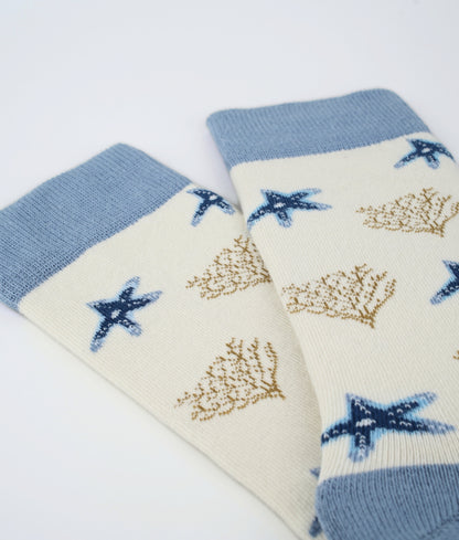 Chaussettes fantaisie crème et bleues à motif d’étoiles de mer beige. Fabriquées en Europe en coton biologique, elles apportent confort, douceur et une touche élégante du bord de mer.