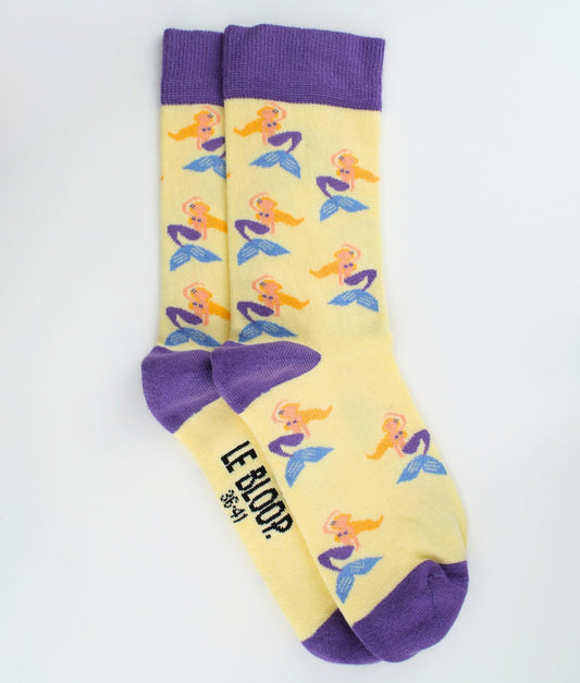 Chaussettes fantaisie jaunes et violettes en coton biologique à motif de sirène. Fabriquées en Europe, elles offrent un confort optimal grâce à leurs zones renforcées et leurs finitions plates sans couture.