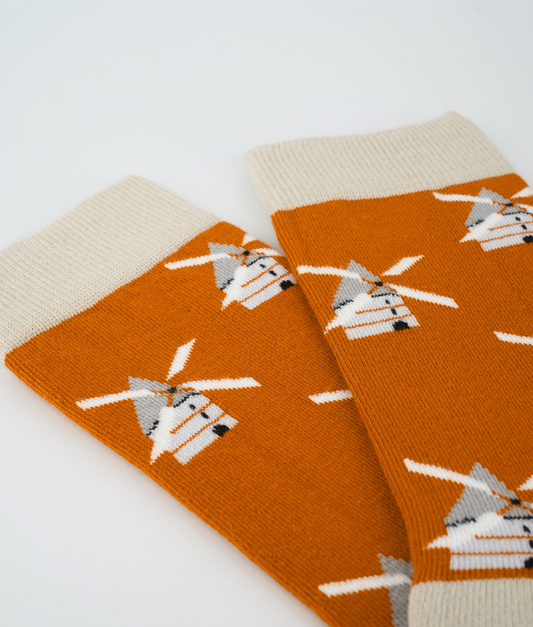 Chaussettes fantaisie orange à motif de moulins à vent. Tricotées en Europe en coton biologique, elles offrent un confort durable grâce à leurs renforts au talon et à la pointe ainsi qu'à leurs finitions plates sans couture.