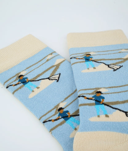 Chaussettes fantaisie bleu clair et beige à motif de sauniers. Fabriquées en Europe en coton biologique, elles offrent confort, douceur et un clin d’œil au savoir-faire local.